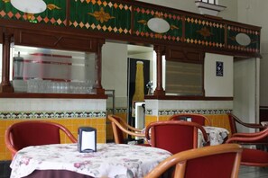 A restaurant interior with a tiled wall, wooden chairs, a table with a floral tablecloth, and a decorative ceiling.