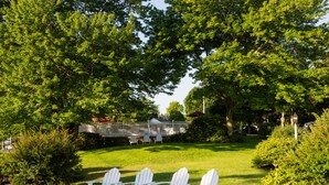 Un jardin avec des chaises blanches, une terrasse en bois et une maison en arrière-plan.