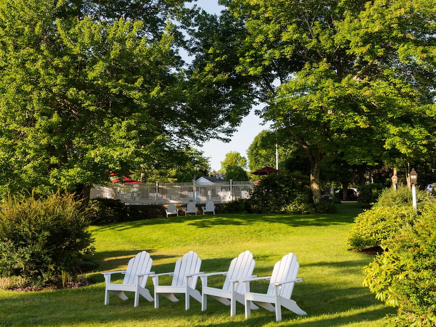 A garden with white chairs, a wooden deck, and a house in the background.