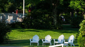 Three white Adirondack chairs on a grassy lawn with a white picket fence in the background.