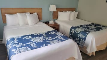 Twee tweepersoonsbedden met houten hoofdborden, witte beddengoed en blauwe bloemenbedspreien in een kamer met lichtblauwe wanden en een houten vloer.
