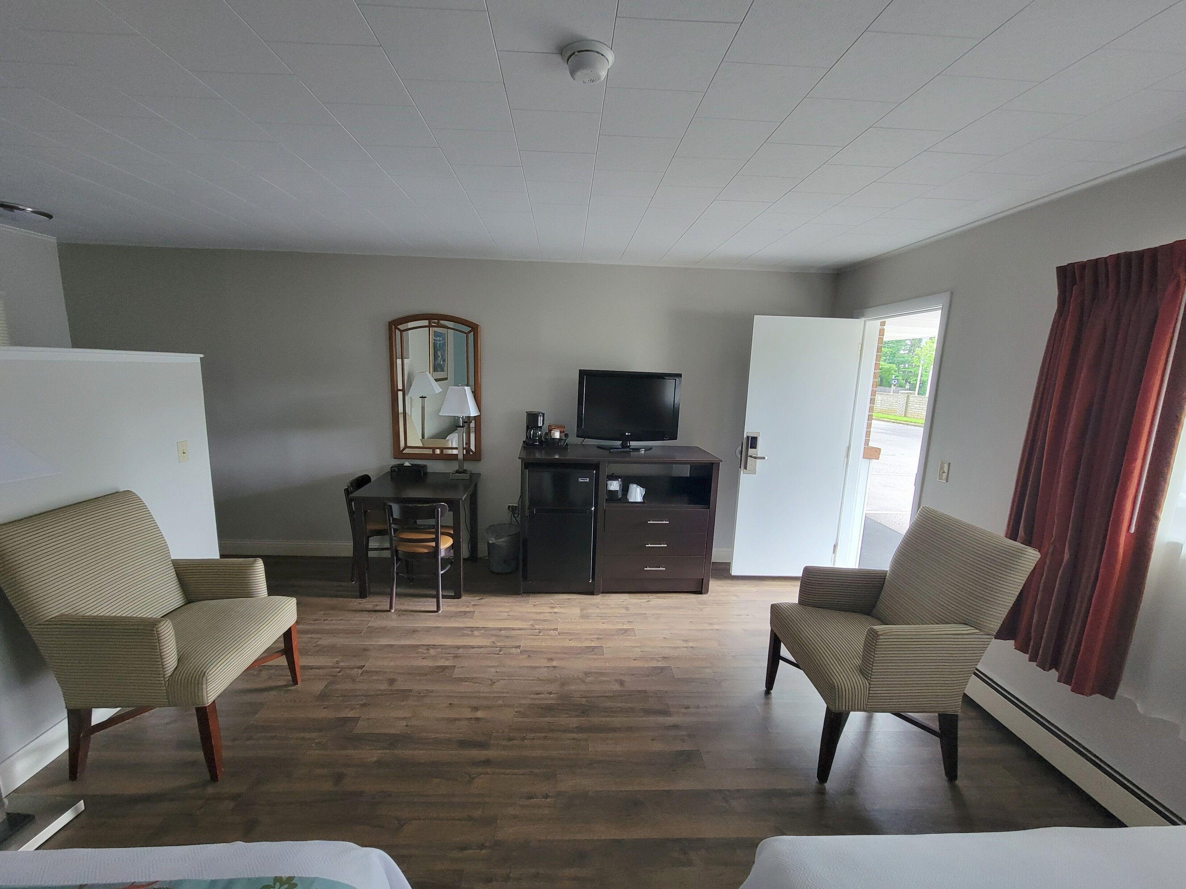 A hotel room with a desk, two chairs, a television, a mirror, and a door leading outside.