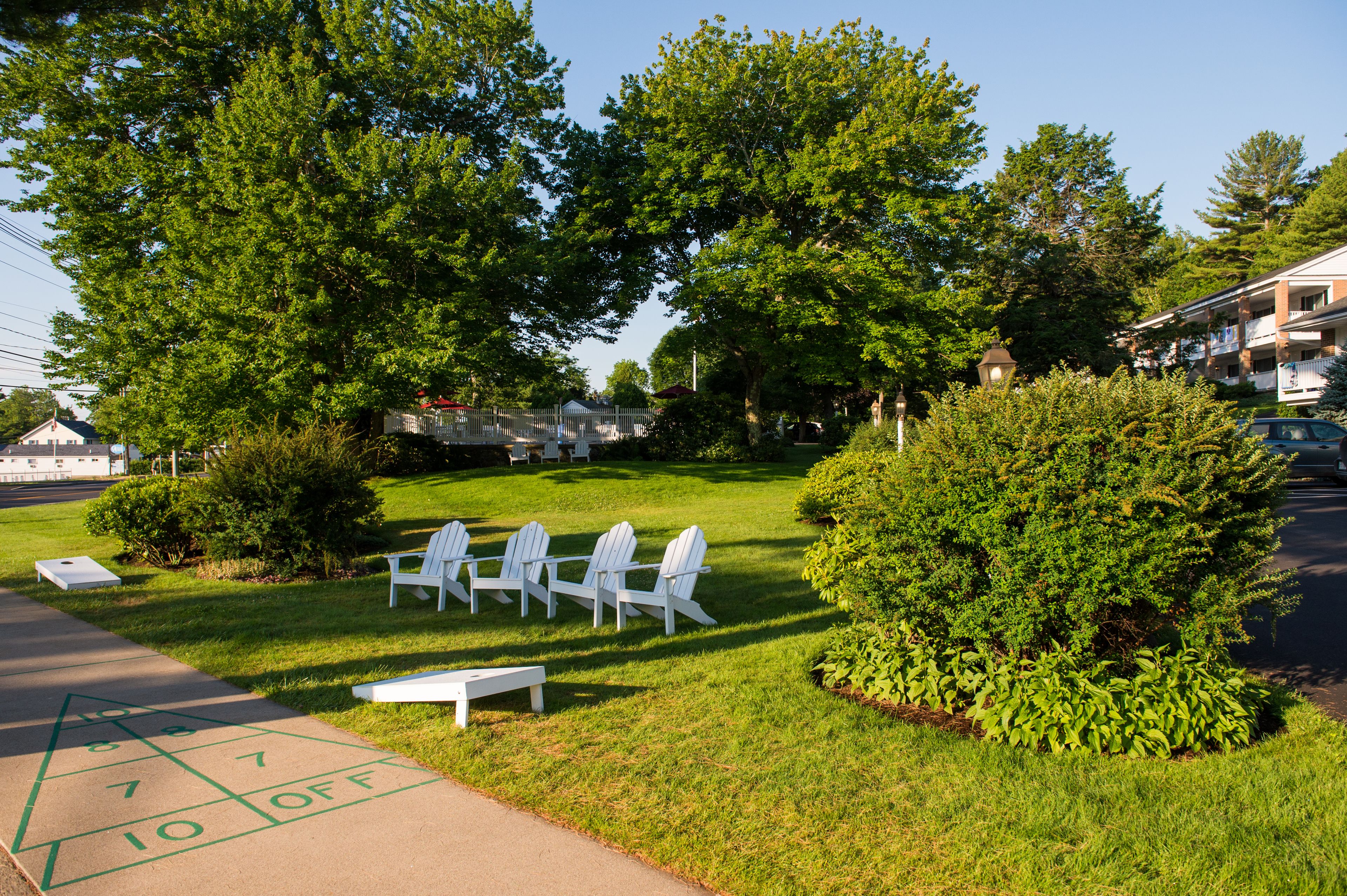 Zona verde con sillas Adirondack blancas y una cancha de juego de shuffleboard.