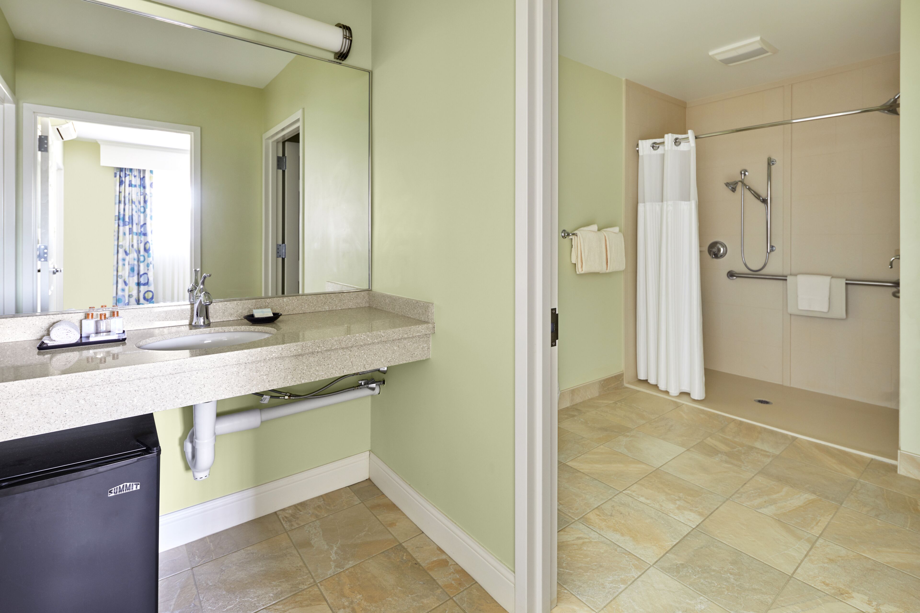 A bathroom with a sink, mirror, towel rack, shower, and toilet.