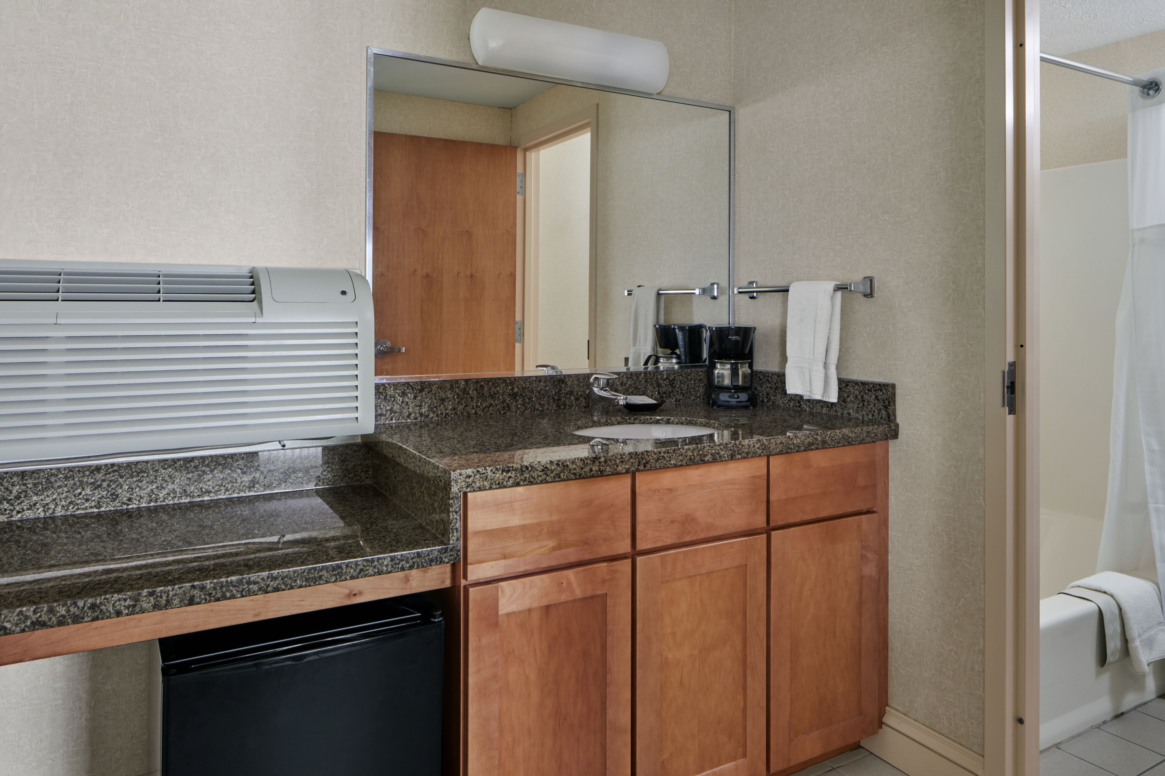 A bathroom with a granite countertop, wooden cabinets, a sink, a coffee maker, and a shower curtain.