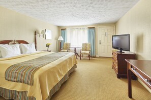 A hotel room with a bed, a television, a desk, two chairs, a lamp, and a window with curtains.