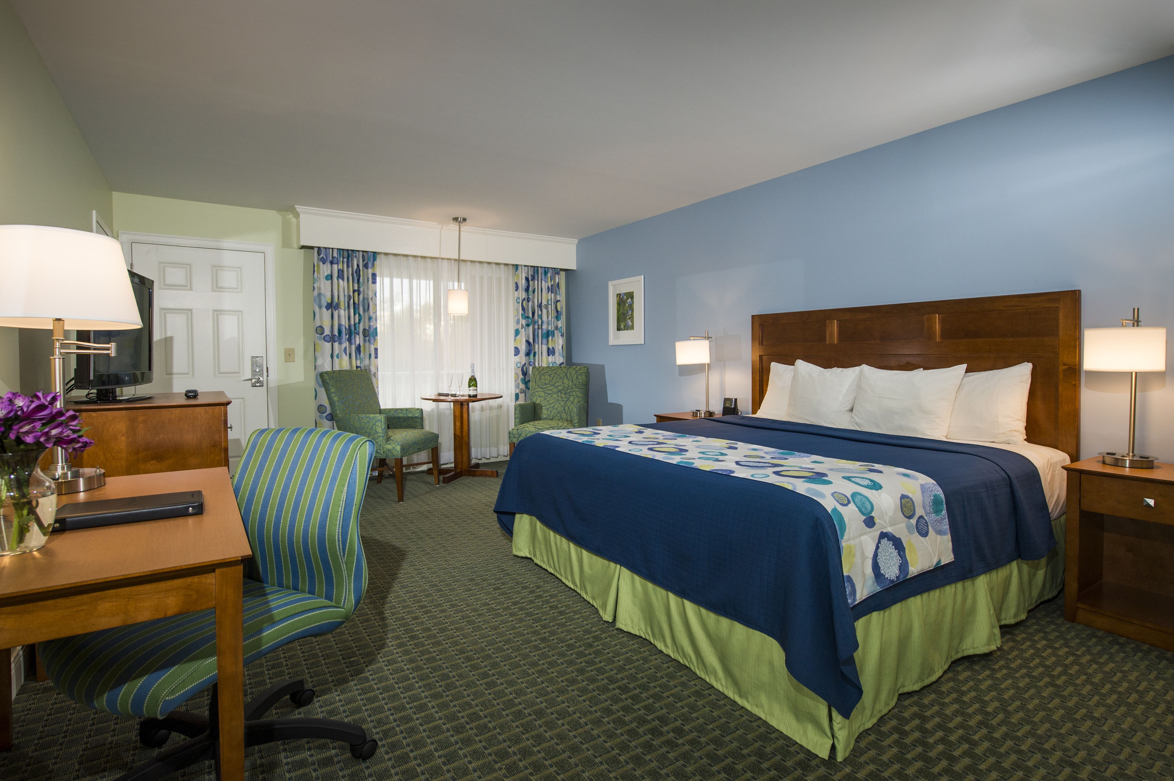 A hotel room with a bed, desk, chair, and a TV.