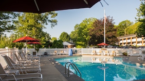 Une piscine entourée d’une clôture blanche et d’arbres, avec des chaises longues et des parasols à proximité.