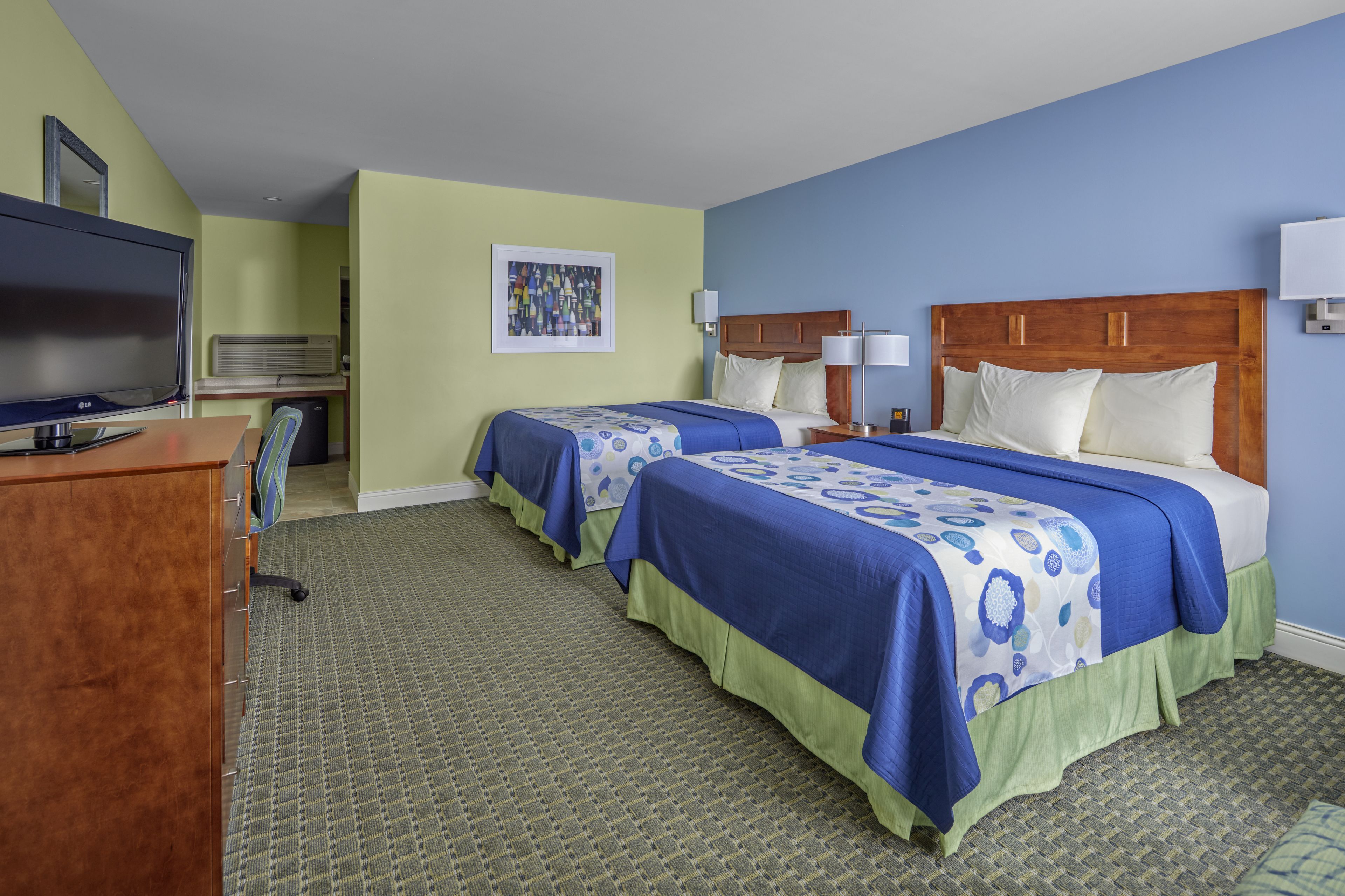A hotel room with two beds, a desk with a television, and a small seating area.