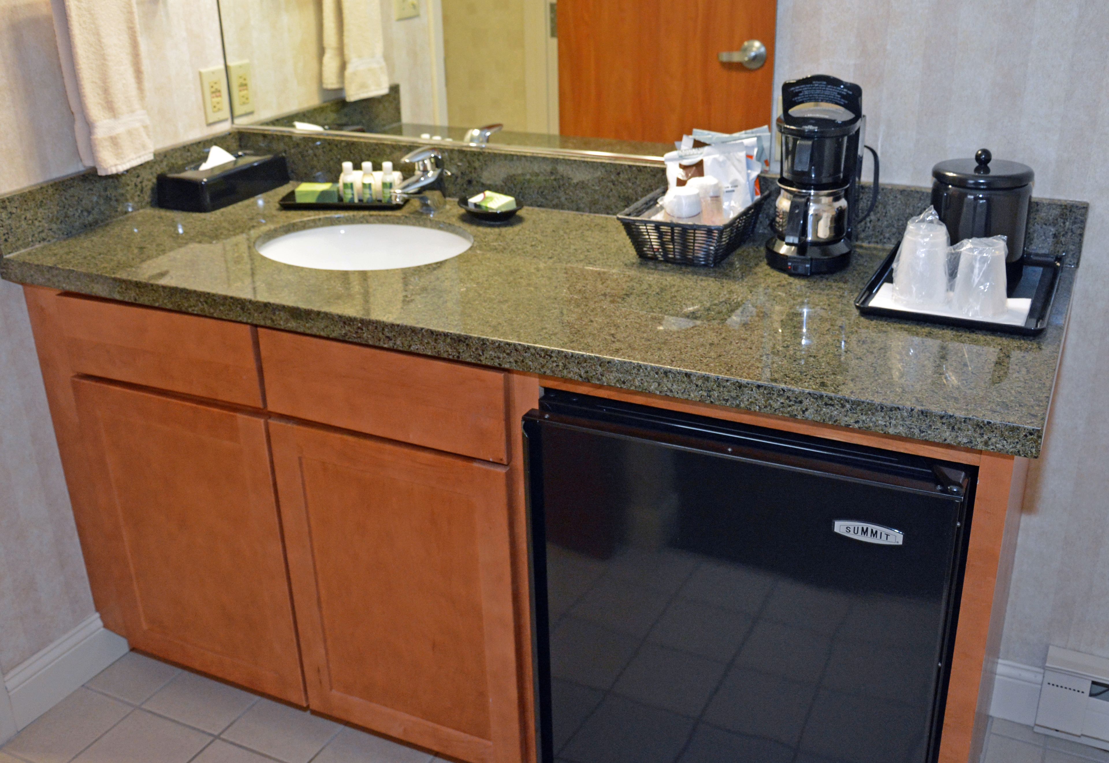 A hotel bathroom with a granite countertop, sink, and a black refrigerator labeled "SUMMIT".