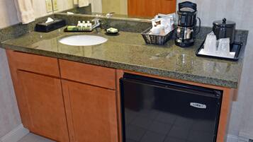 A hotel bathroom with a granite countertop, sink, and a black refrigerator labeled "SUMMIT".