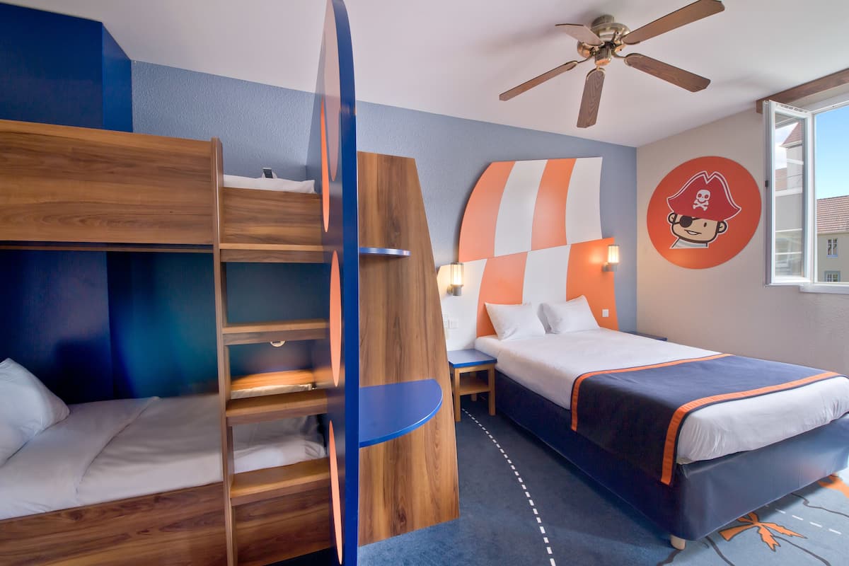 A hotel room with bunk beds, a desk, a ceiling fan, and a wall with a pirate-themed decoration.