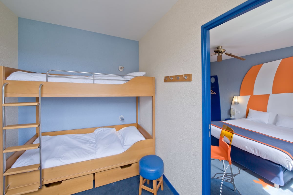 A hotel room with a bunk bed, a single bed, a desk with a chair, and a mirror.