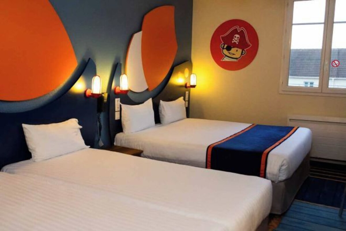 A hotel room with two beds, a large abstract wall design, and a cartoon pirate logo on the wall.