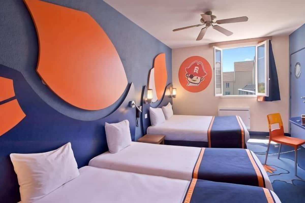 A hotel room with two beds, a ceiling fan, a window with a view, and a wall clock.