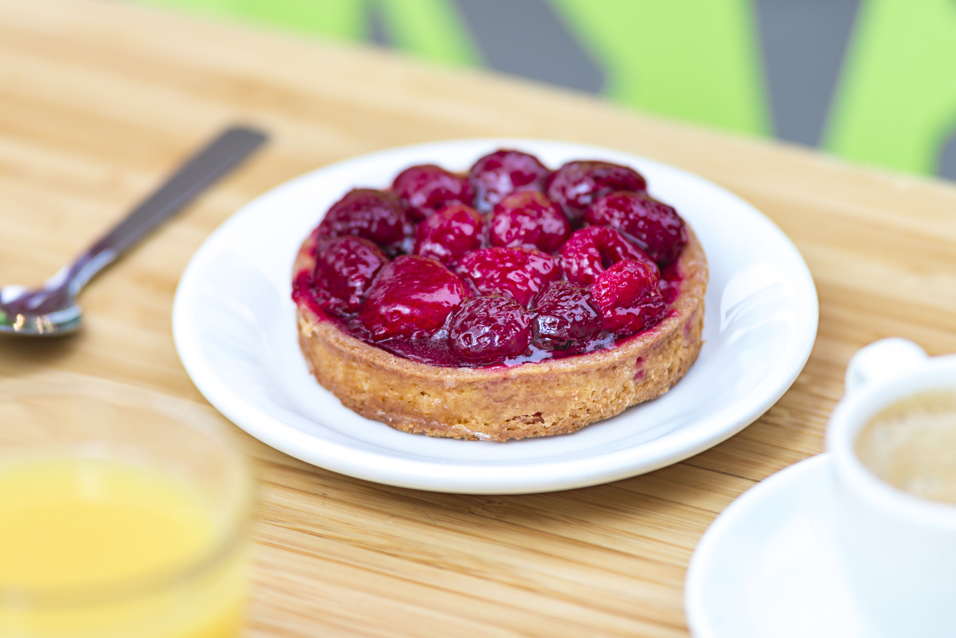 Ein runder Obstkuchen auf einem weißen Teller mit einem Löffel und einer Tasse Kaffee auf einem Holztisch.