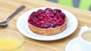 Ein runder Obstkuchen auf einem weißen Teller mit einem Löffel und einer Tasse Kaffee auf einem Holztisch.