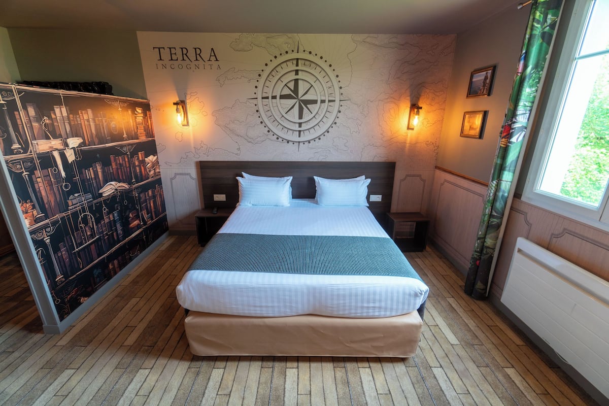 A neatly made bed with a headboard, a wall map, and two wall-mounted lamps.