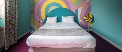 A bed with white bedding, a colorful abstract wall mural, and a lollipop-shaped decoration.