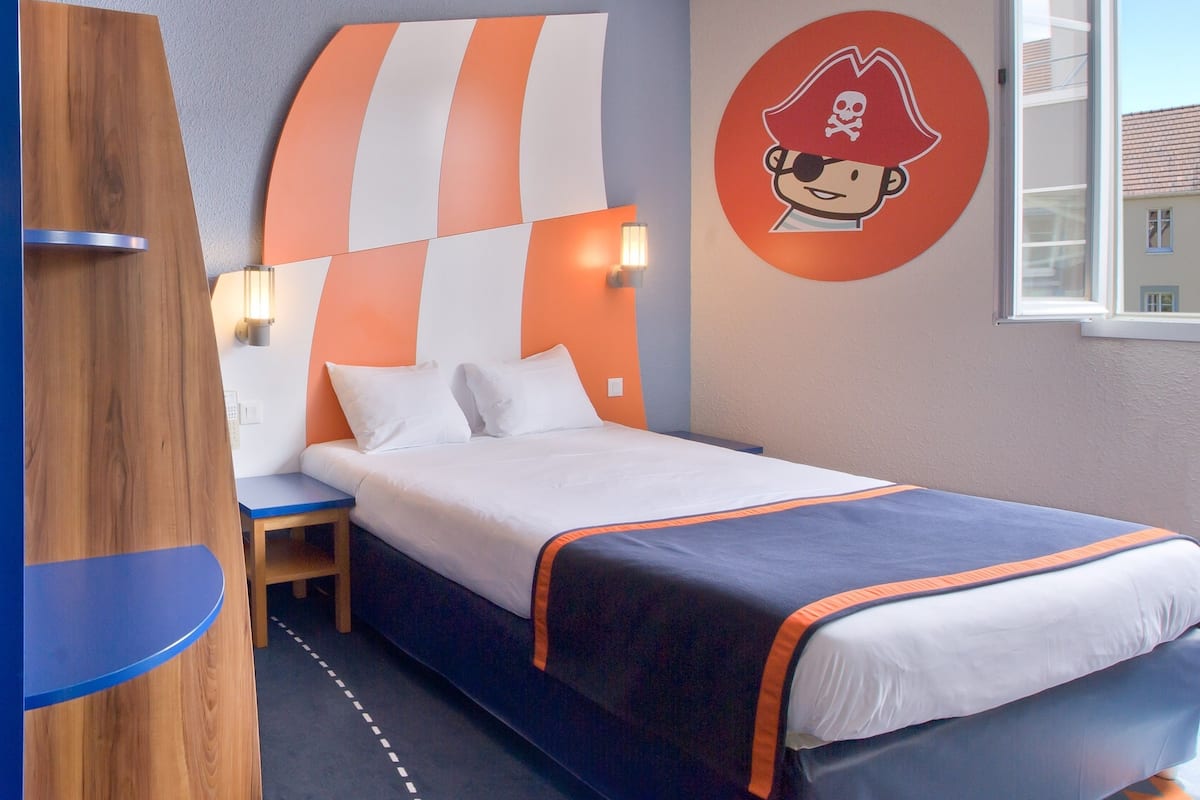 A bedroom with a bed, a nightstand, a wall clock, and a window.