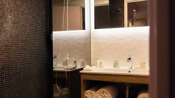 A modern bathroom with a glass shower enclosure, a white sink with a mirror above it, and neatly folded towels on a shelf.