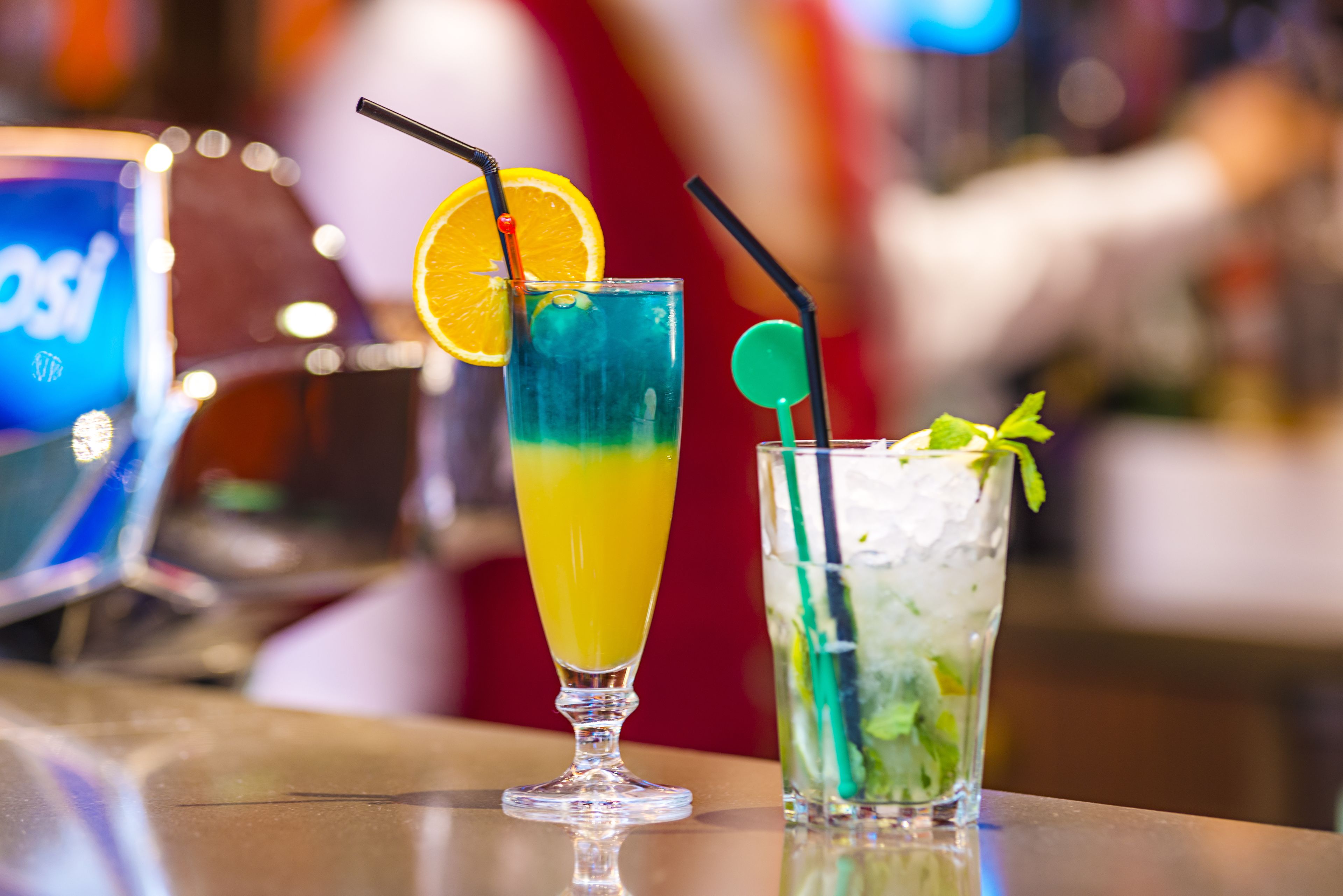 Two cocktails on a bar counter with a blurred background.