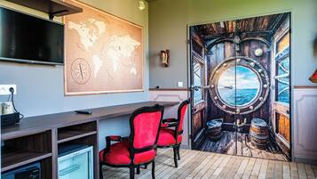 A room with a large world map, a TV, a desk, and a door with a maritime theme.