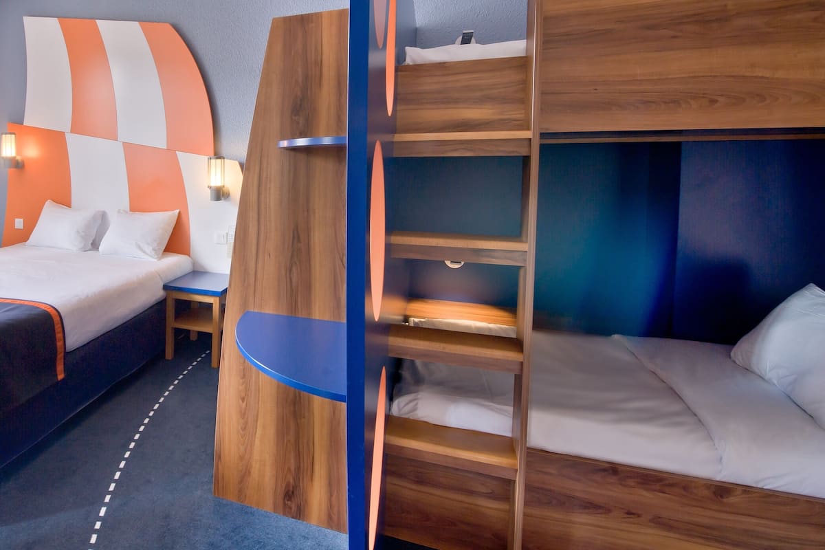 A hotel room with bunk beds, a wooden headboard, a bedside table, and a lamp.