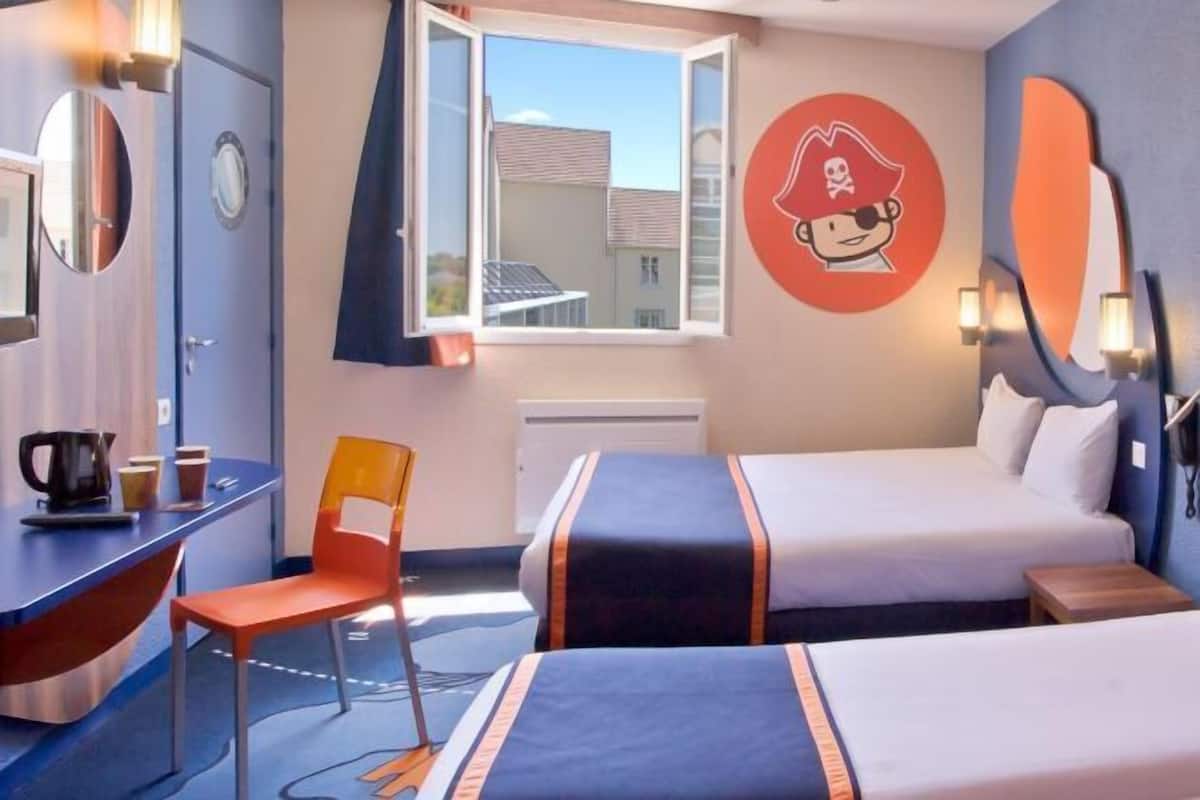 A hotel room with two beds, a desk, a chair, a window, and a wall with a pirate-themed decoration.