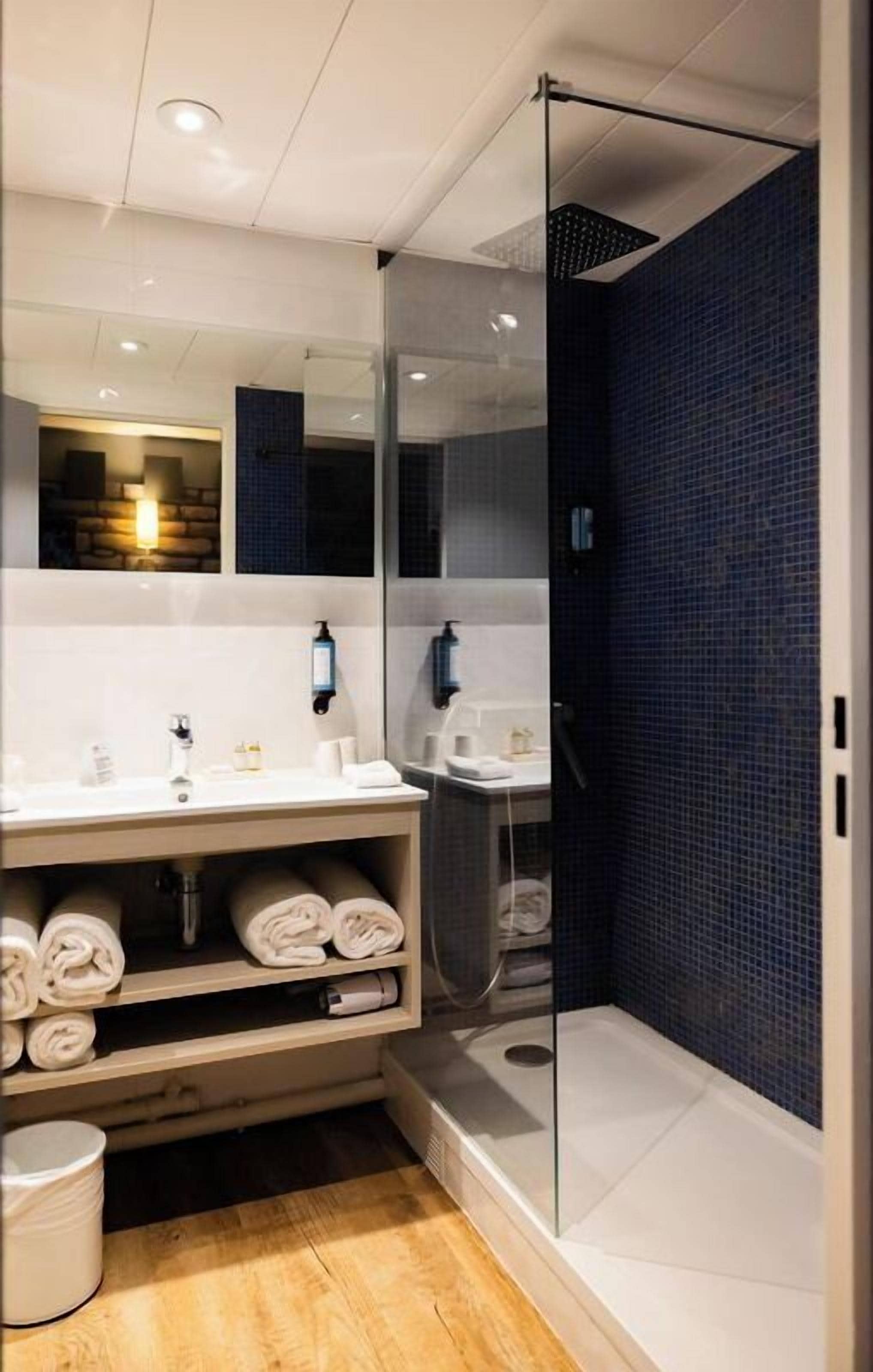 Une salle de bain moderne avec une douche à parois de verre, des accessoires blancs et un mur recouvert de carreaux bleu foncé.