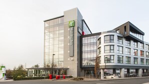 A modern hotel building with a prominent glass facade, a green logo, and a curved corner design. - Holiday Inn London - West by IHG (London)