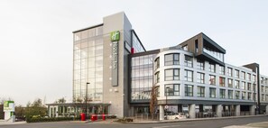 Een modern hotelgebouw met een opvallende glazen gevel, een groen logo en een gebogen hoek.