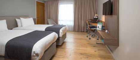 A hotel room with two beds, a desk with a chair, a TV, and a large window with curtains.