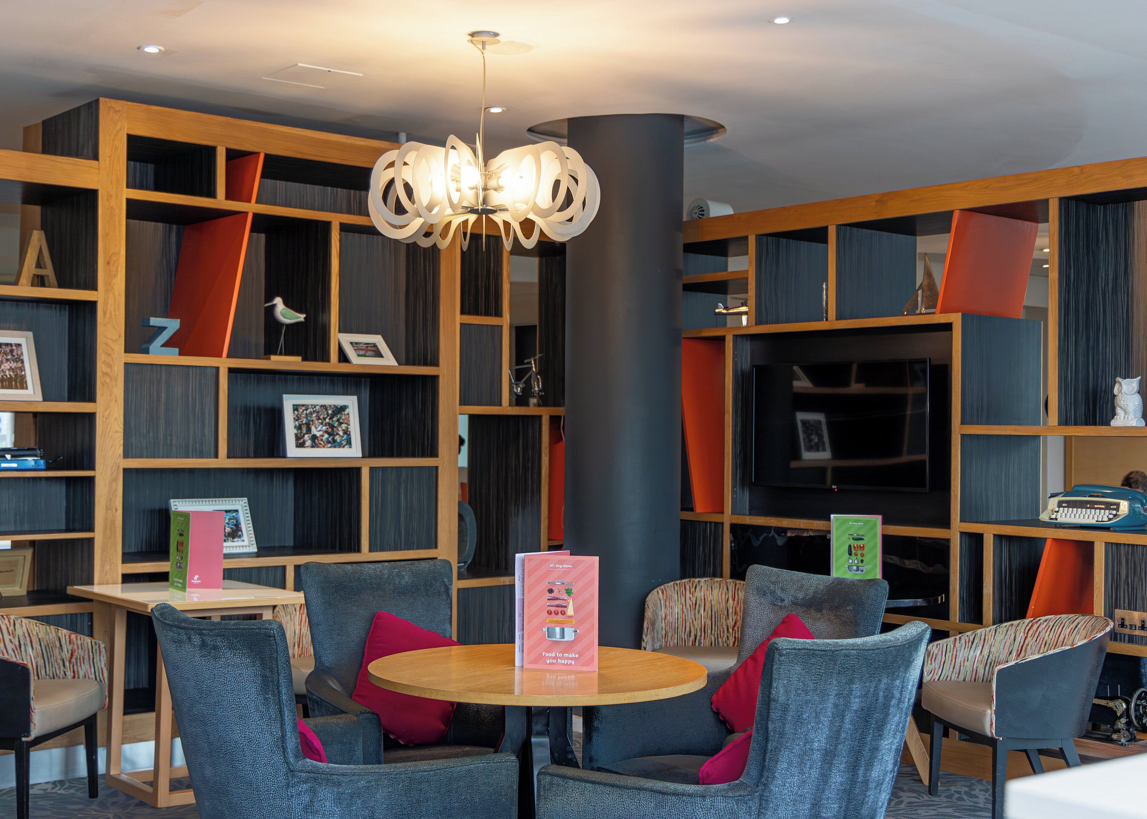 A modern library with bookshelves, a round wooden table, and comfortable seating.