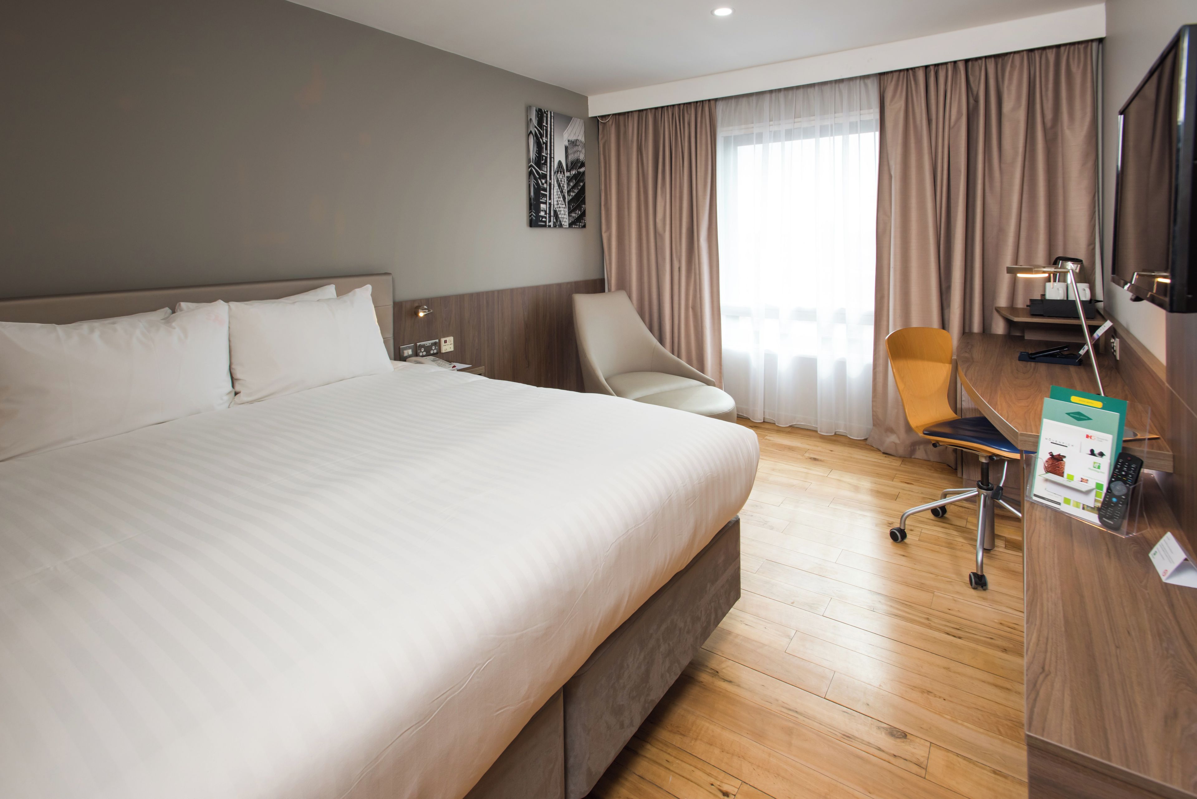 Een hotelkamer met een groot bed, een bureau met stoel, een televisie en een raam met gordijnen.