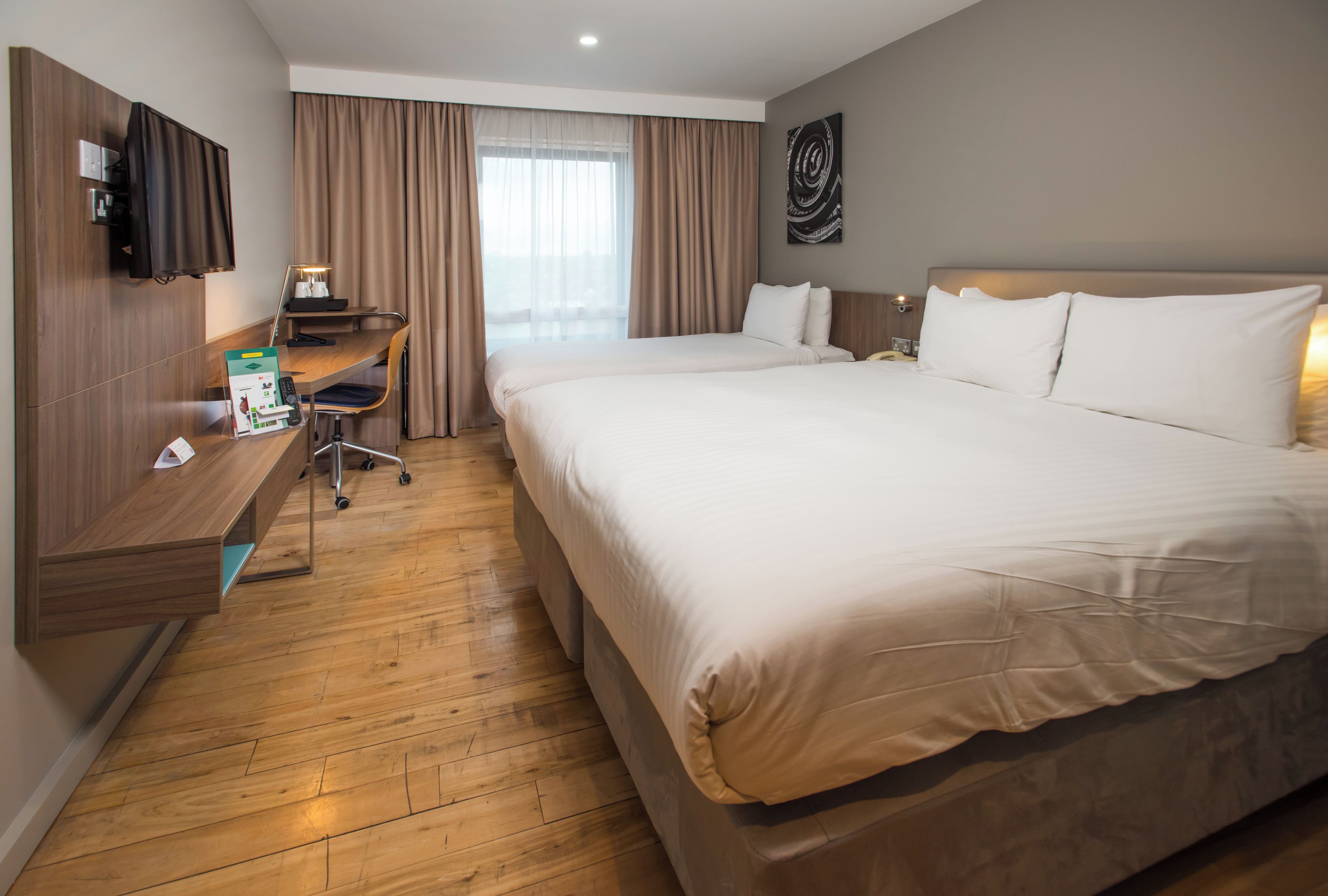 Een hotelkamer met een groot bed, een bureau met lamp, een televisie en een raam met gordijnen.
