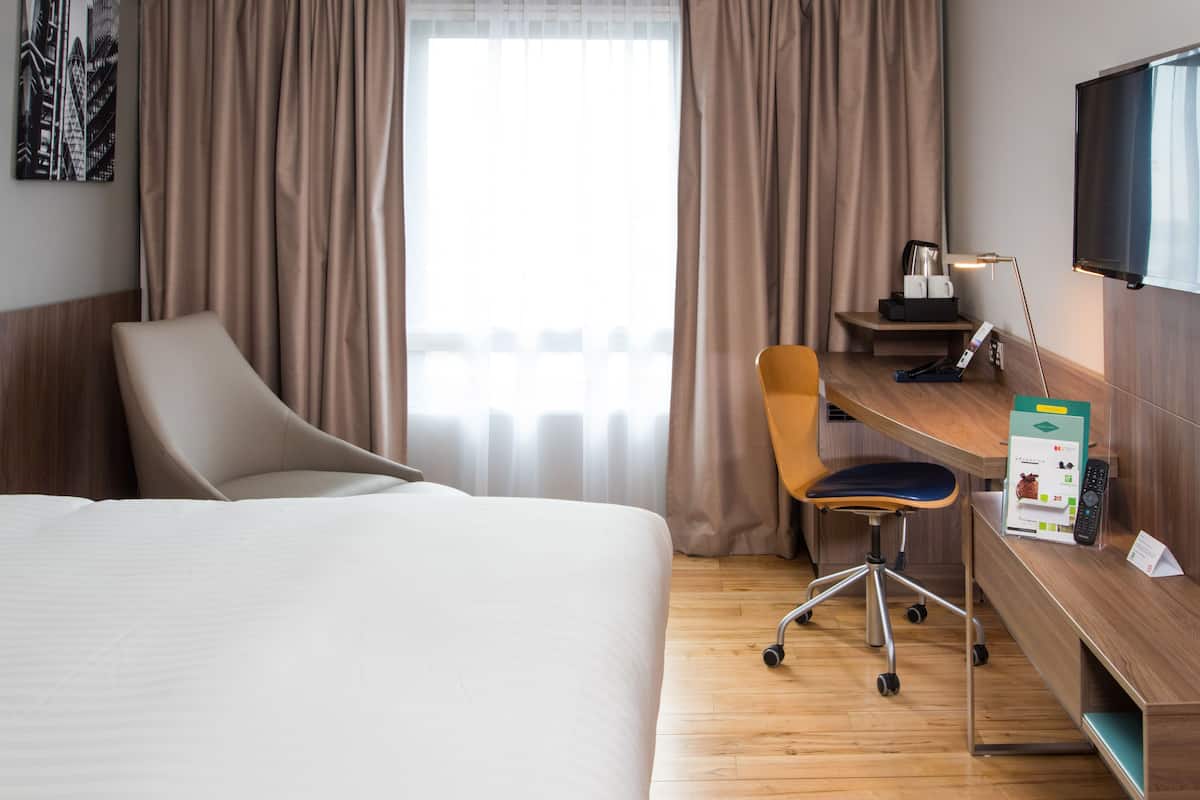 Ein Hotelzimmer mit Bett, Schreibtisch mit Stuhl, Fernseher und einem Fenster mit Vorhängen.