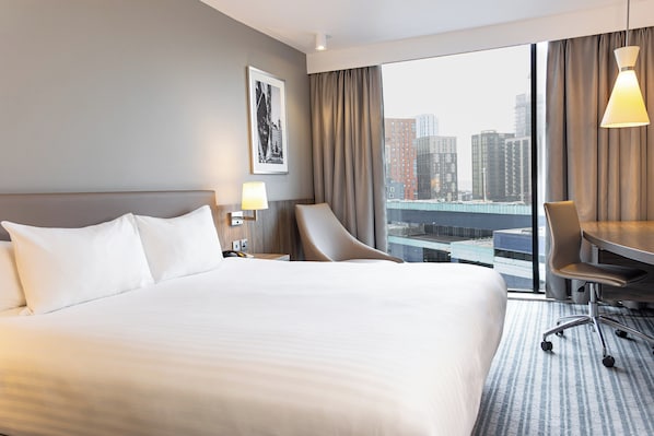 Hotelkamer met een groot bed, een bureau, een stoel en uitzicht op een stadslandschap.
