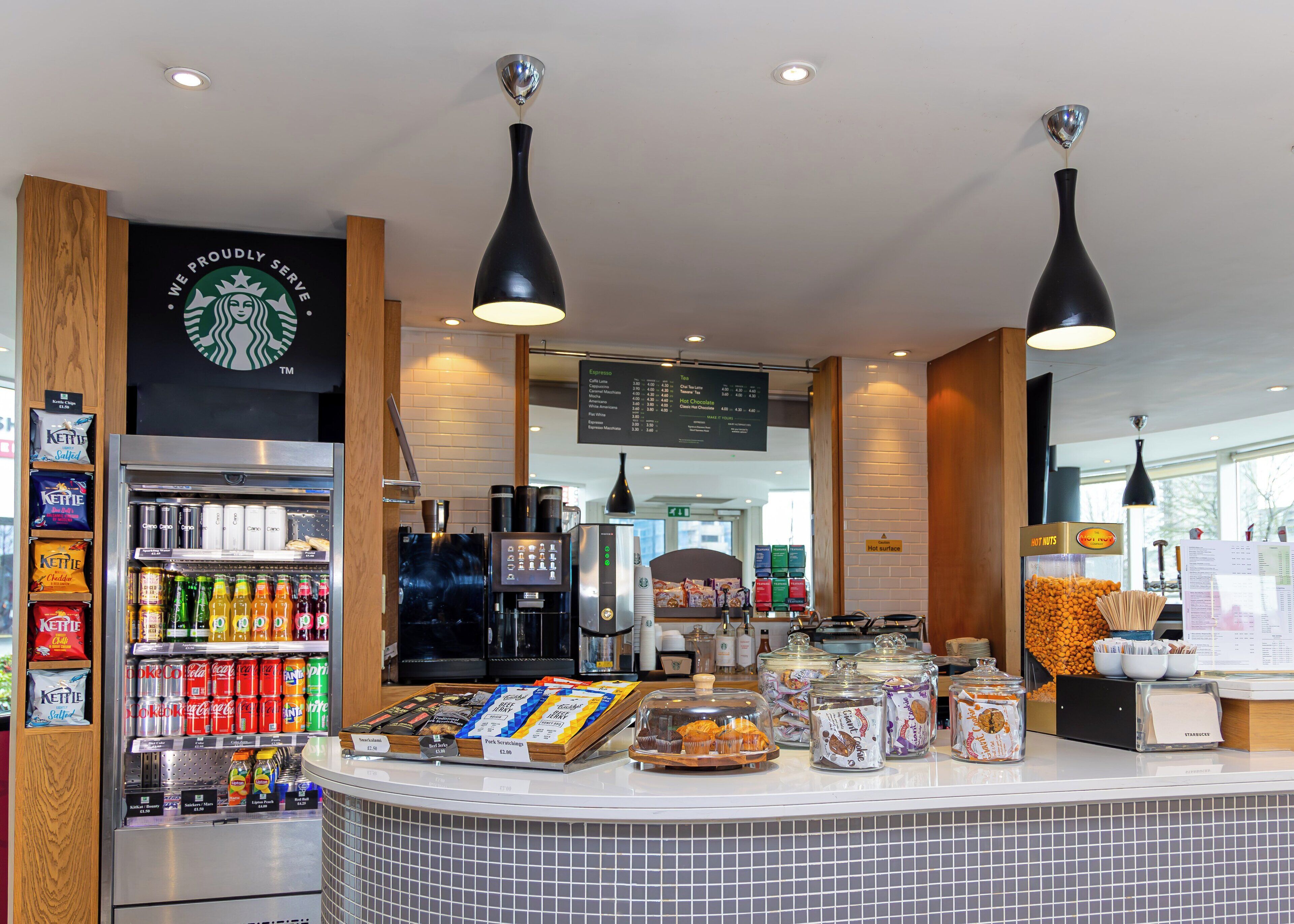 A Starbucks coffee shop interior with a self-serve beverage station, menu board, and various food items.