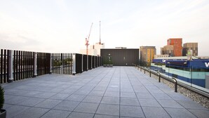 A rooftop terrace with a tiled floor, a metal fence, and a view of the city skyline including buildings and a construction crane. - Holiday Inn London - West by IHG (London)