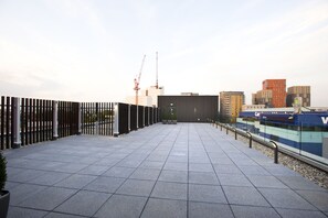 Een dakterras met betegelde vloer, een metalen hek en uitzicht op de stadshemel, inclusief gebouwen en een bouwkraan.
