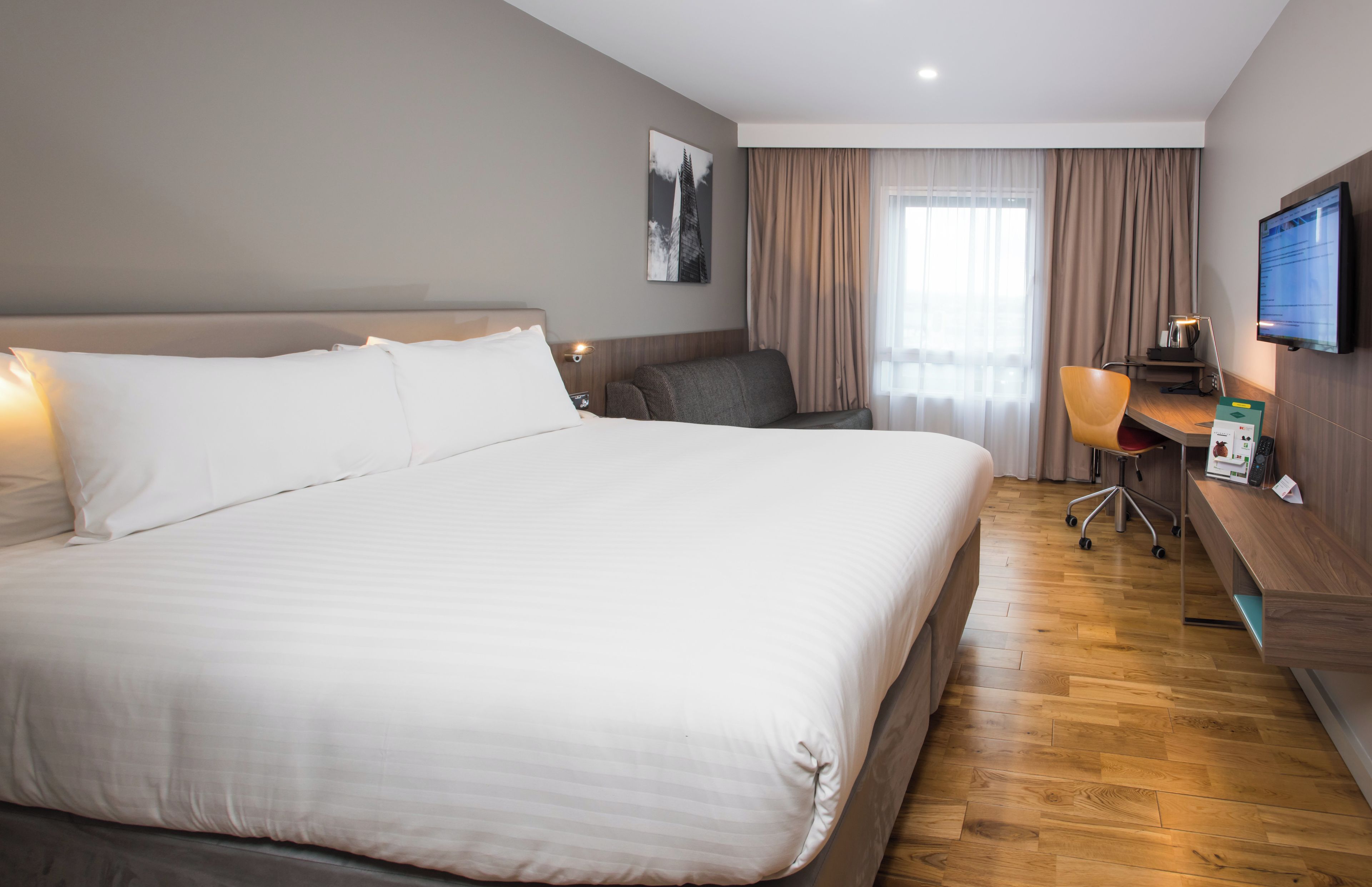 Een hotelkamer met een groot bed, een bureau, een stoel, een televisie en een raam met gordijnen.