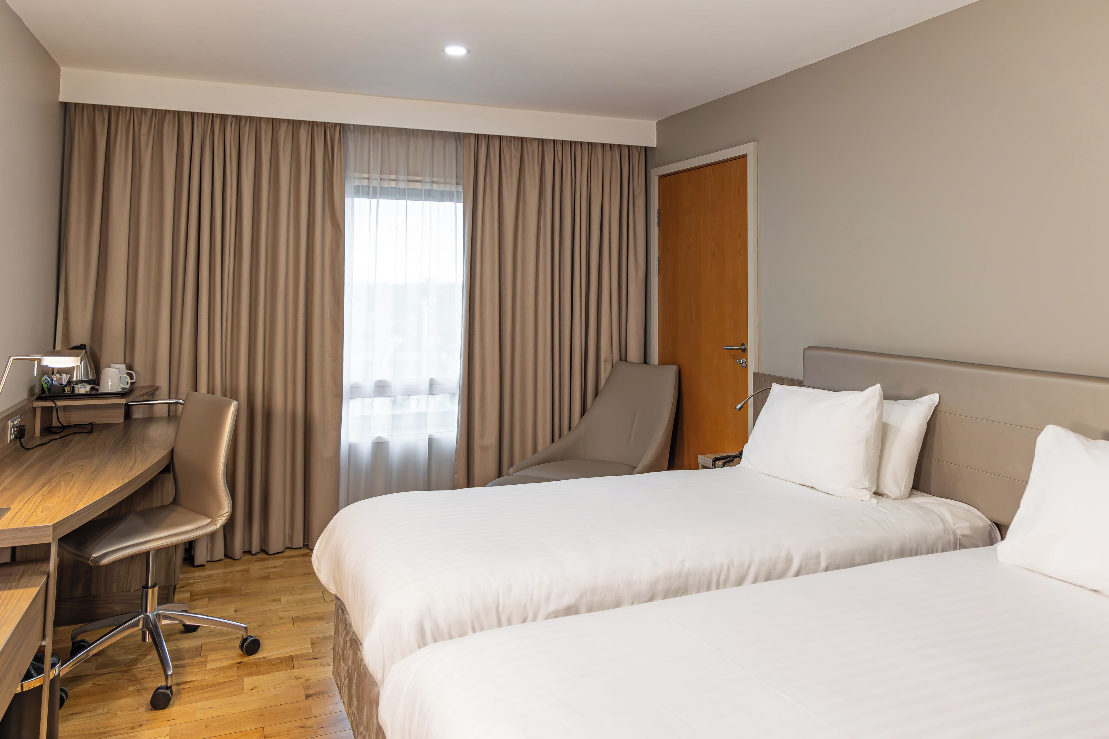 Habitació d'hotel amb dos llits, un escriptori, una cadira i un armari.