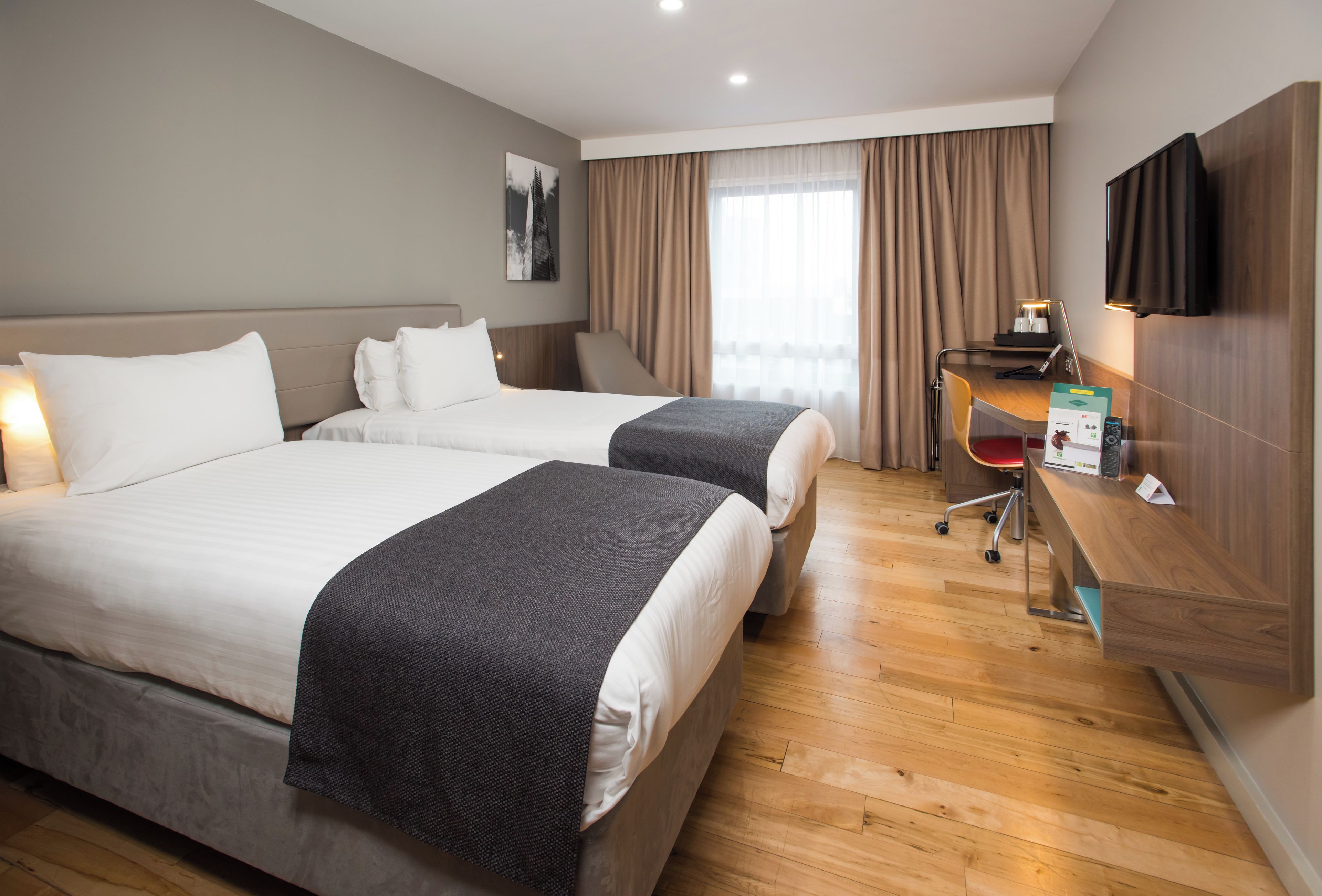 A hotel room with two beds, a desk with a computer, a chair, and a TV mounted on the wall.