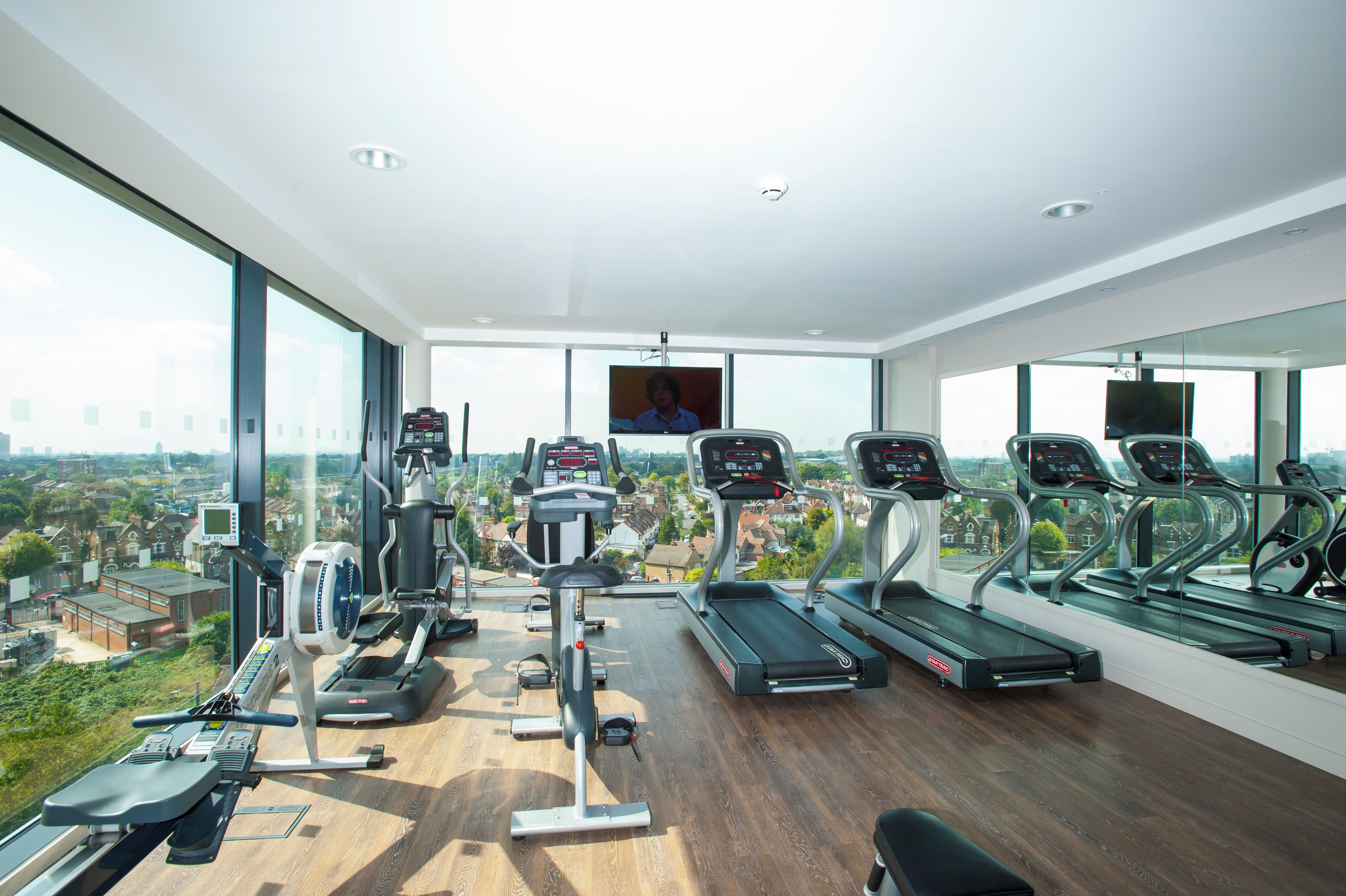 A gym with various exercise equipment, large windows, and a view of a cityscape.
