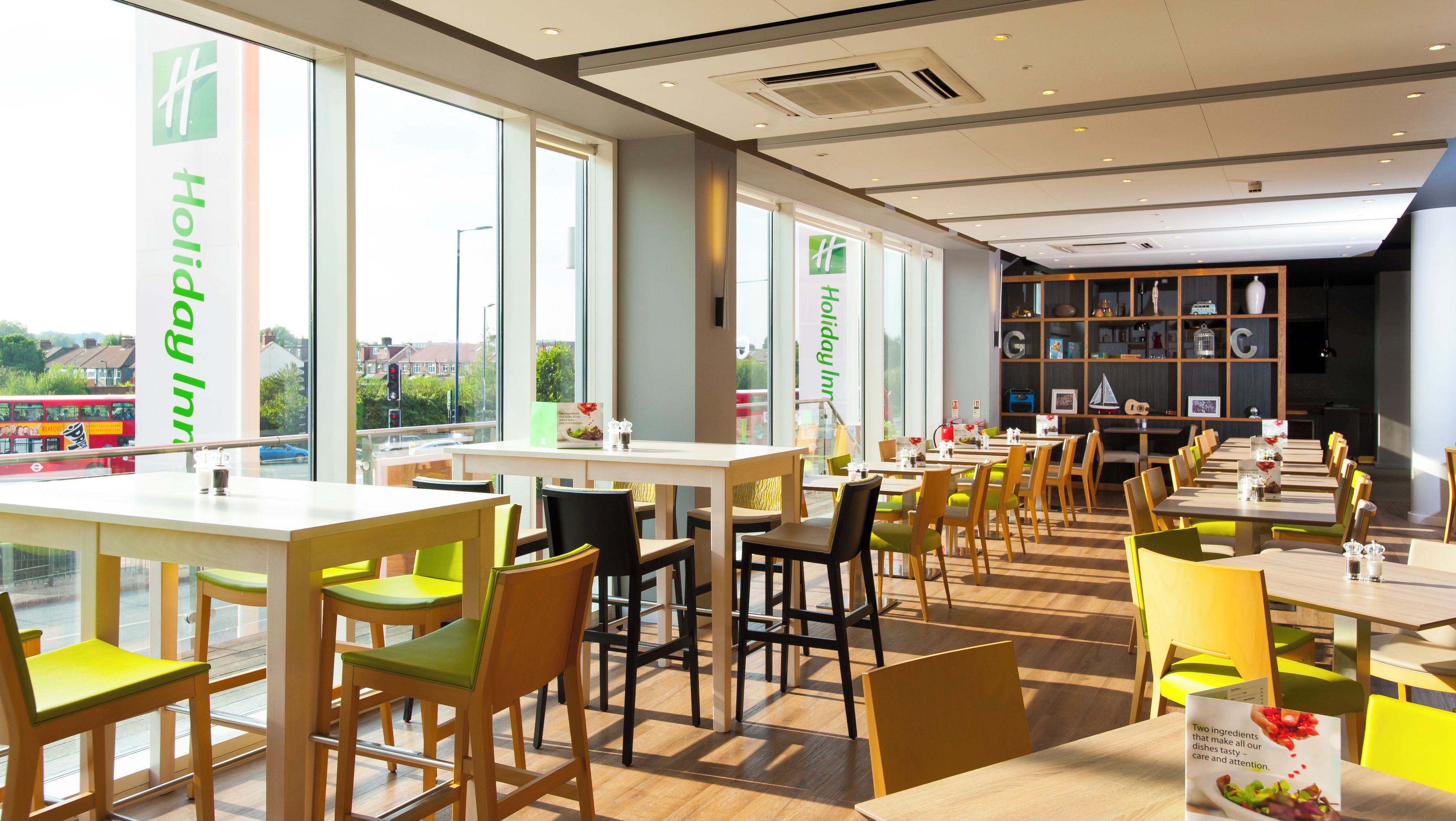A modern restaurant with multiple tables and chairs, large windows, and a view of the outside.