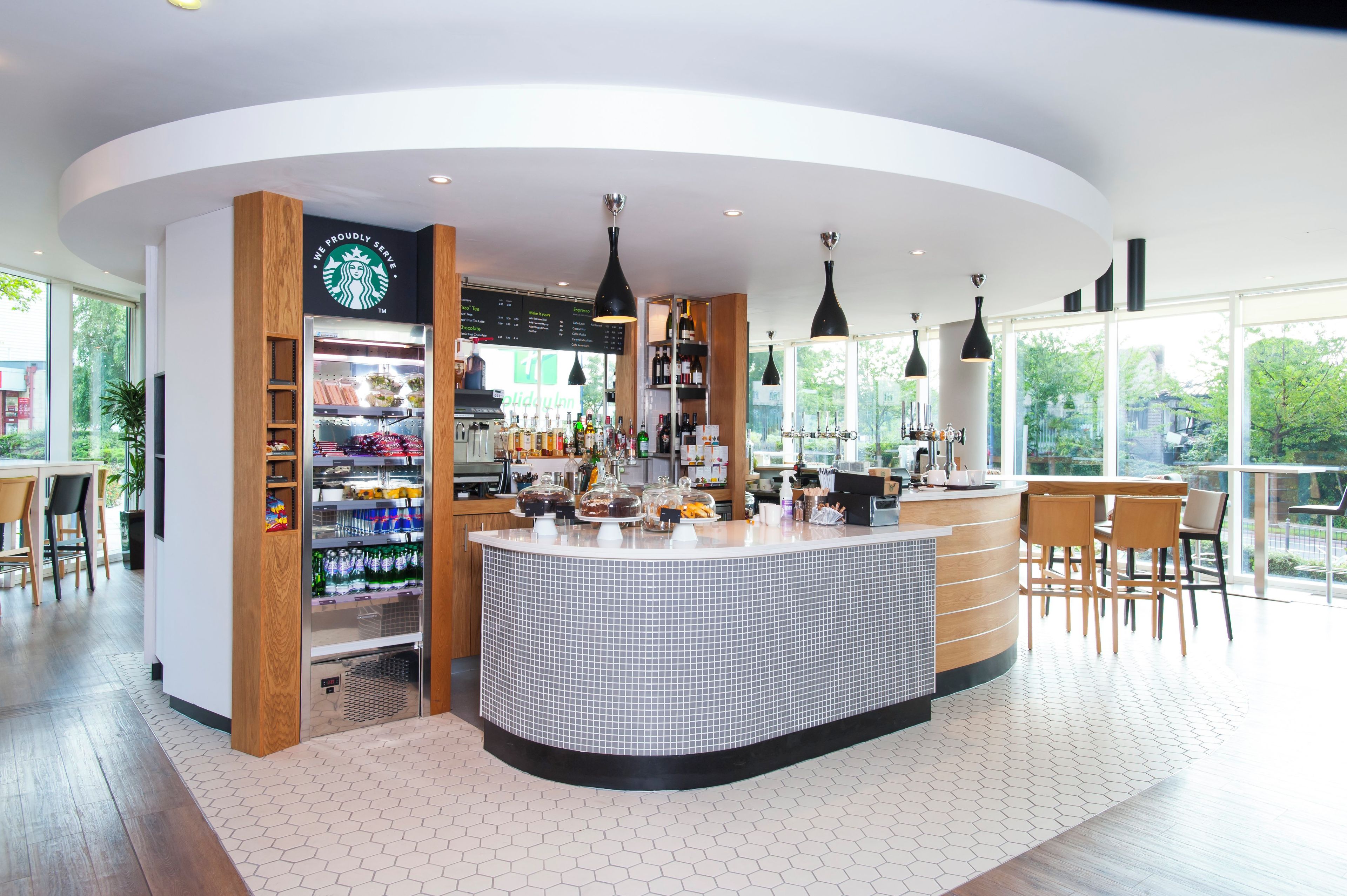 A modern coffee shop with a central counter, a Starbucks sign, and a menu board.