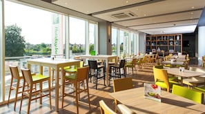 A modern restaurant with large windows, wooden tables, and chairs. - Holiday Inn London - West by IHG (London)