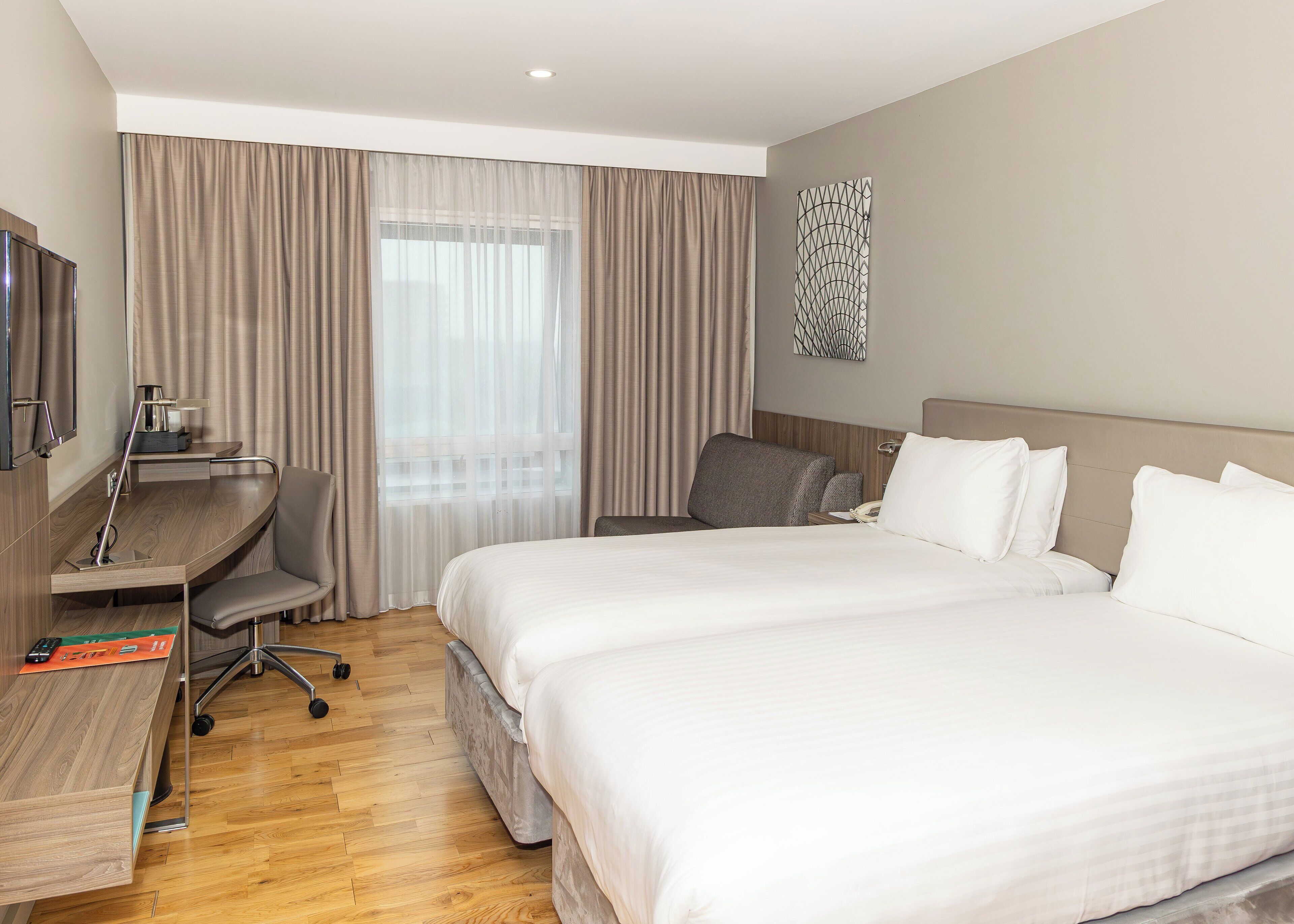 A hotel room with a bed, a desk, a chair, a TV, and a window with curtains.