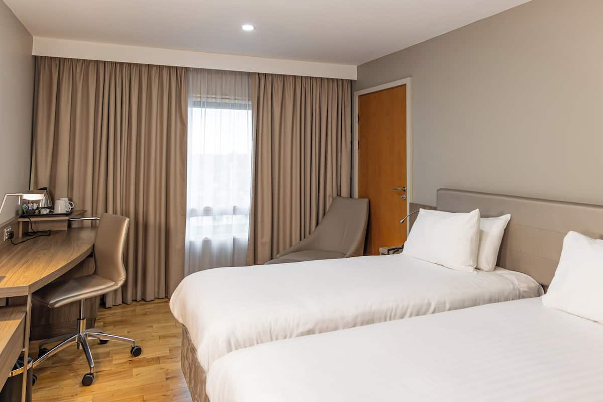 Ein Hotelzimmer mit zwei Betten, einem Schreibtisch, einem Stuhl und einem Kleiderschrank.